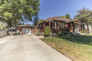 View of front facade with brick siding, a garage, driveway, a front yard, and an outbuilding
