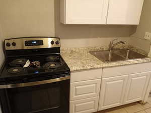 Kitchen featuring stainless steel range with electric cooktop, white cabinets, light stone counters, and light tile patterned flooring