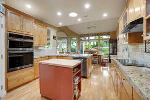 Kitchen featuring light wood finished floors, a peninsula, butcher block counters, appliances with stainless steel finishes, and light brown cabinets