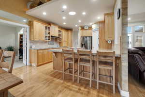 Kitchen with backsplash, light wood-type flooring, glass insert cabinets, a peninsula, and light brown cabinets