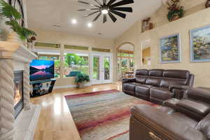 Living room featuring ceiling fan, french doors, wood finished floors, a glass covered fireplace, and high vaulted ceiling