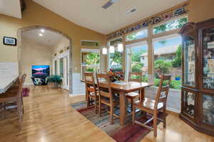 Dining space with arched walkways, light wood finished floors, and high vaulted ceiling