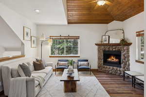 Living room featuring a stone fireplace, ceiling fan, wood ceiling, wood finished floors, and lofted ceiling