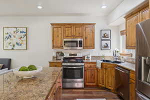Kitchen featuring appliances with stainless steel finishes, dark wood-style floors, brown cabinets, recessed lighting, and light stone countertops