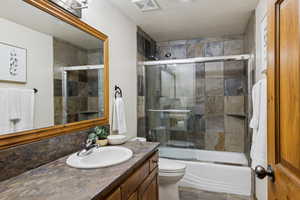 Full bath featuring vanity, combined bath / shower with glass door, and a textured ceiling