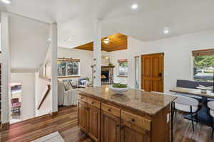 Kitchen featuring open floor plan, ceiling fan, a fireplace, dark wood-style flooring, and stone counters