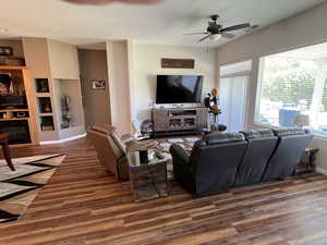 Living room featuring wood finished floors, a ceiling fan, a glass covered fireplace, built in shelves, and a textured ceiling