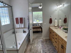 Ensuite bathroom featuring double vanity, a garden tub, ceiling fan, and plenty of natural light