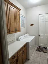 Washroom featuring cabinet space, washing machine and dryer, light tile patterned floors, and a textured ceiling