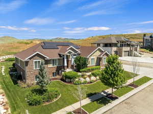 View of front of property featuring concrete driveway, roof mounted solar panels, stone siding, roof with shingles, and a front yard