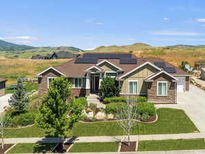 Craftsman-style house featuring stone siding, board and batten siding, driveway, a mountain view, and roof mounted solar panels