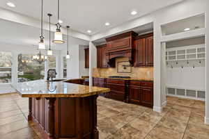 Kitchen featuring decorative light fixtures, tasteful backsplash, light stone counters, recessed lighting, and a kitchen breakfast bar