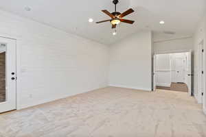 Empty room featuring lofted ceiling, wooden walls, a ceiling fan, light colored carpet, and recessed lighting