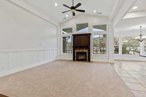 Unfurnished living room with plenty of natural light, a decorative wall, high vaulted ceiling, a chandelier, and a fireplace with flush hearth