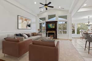 Living area with a glass covered fireplace, high vaulted ceiling, a ceiling fan, a chandelier, and recessed lighting
