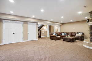 Living area featuring carpet, stairs, recessed lighting, and a stone fireplace