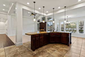 Kitchen featuring pendant lighting, dark brown cabinetry, an island with sink, light stone countertops, and recessed lighting