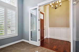 Unfurnished dining area with a chandelier, dark wood-style floors, and a wainscoted wall