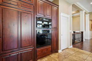 Kitchen with light tile patterned floors, decorative columns, crown molding, and dark brown cabinets