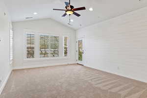 Carpeted spare room featuring vaulted ceiling, a ceiling fan, and wood walls