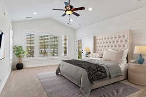 Carpeted bedroom with wood walls, vaulted ceiling, and ceiling fan
