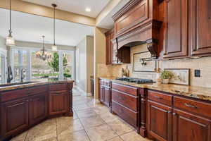 Kitchen featuring gas stovetop, tasteful backsplash, a chandelier, decorative light fixtures, and light stone counters
