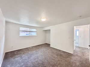 Unfurnished bedroom with dark carpet, multiple windows, a closet, and a textured ceiling