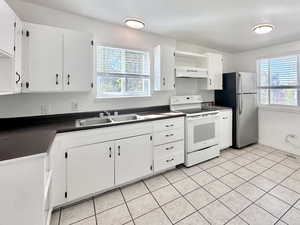 Kitchen with dark countertops, white range with electric cooktop, white cabinetry, healthy amount of natural light, and a textured ceiling