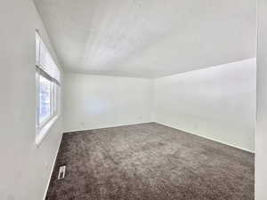 Unfurnished room featuring dark colored carpet and a textured ceiling
