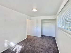 Unfurnished bedroom with dark carpet, a textured ceiling, and a closet
