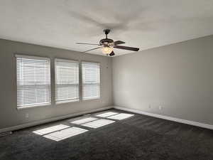 Empty room featuring dark colored carpet, ceiling fan, healthy amount of natural light, and a textured ceiling