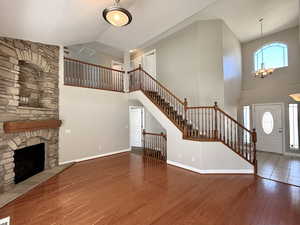 Foyer entrance featuring high vaulted ceiling, hardwood / wood-style flooring, a chandelier, stairs, and a fireplace