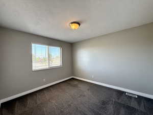 Empty room featuring dark colored carpet and a textured ceiling