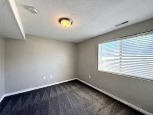 Unfurnished room featuring dark carpet, a smoke detector, and a textured ceiling