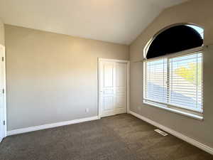 Spare room featuring dark carpet and lofted ceiling