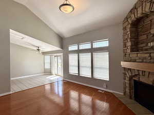 Unfurnished living room with hardwood / wood-style flooring, a stone fireplace, high vaulted ceiling, and a ceiling fan