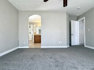 Unfurnished bedroom with carpet floors, arched walkways, ensuite bathroom, and ceiling fan