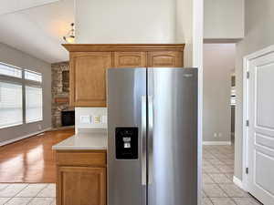 Kitchen featuring stainless steel refrigerator with ice dispenser, light tile patterned flooring, light countertops, and a fireplace