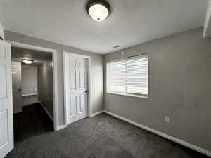 Unfurnished bedroom with dark colored carpet and a textured ceiling