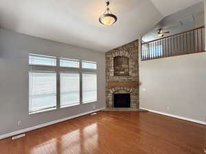 Unfurnished living room with wood finished floors, a ceiling fan, lofted ceiling, and a fireplace
