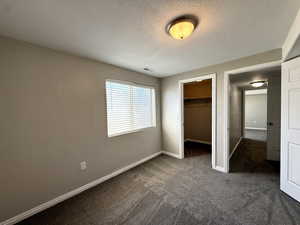 Unfurnished bedroom featuring dark carpet, a textured ceiling, and a walk in closet