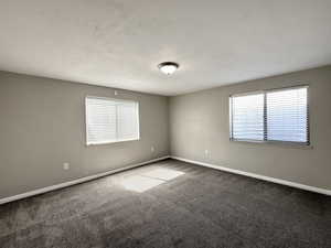 Unfurnished room with plenty of natural light and dark colored carpet