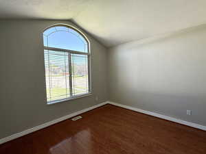 Unfurnished room with wood finished floors, vaulted ceiling, and a textured ceiling