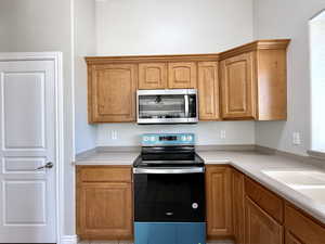 Kitchen featuring stainless steel appliances, light countertops, light tile patterned floors, and brown cabinets