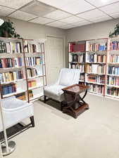 Sitting room with a drop ceiling, wall of books, and carpet floors