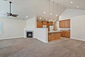 Kitchen with light colored carpet, high vaulted ceiling, open floor plan, ceiling fan, and light countertops