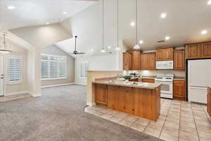 Kitchen with light colored carpet, white appliances, a peninsula, vaulted ceiling, and open floor plan
