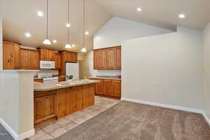 Kitchen featuring white appliances, a peninsula, brown cabinetry, high vaulted ceiling, and pendant lighting