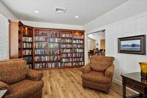 Sitting room with wood finished floors, bookshelves, and recessed lighting