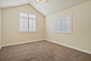 Carpeted spare room featuring a ceiling fan and vaulted ceiling